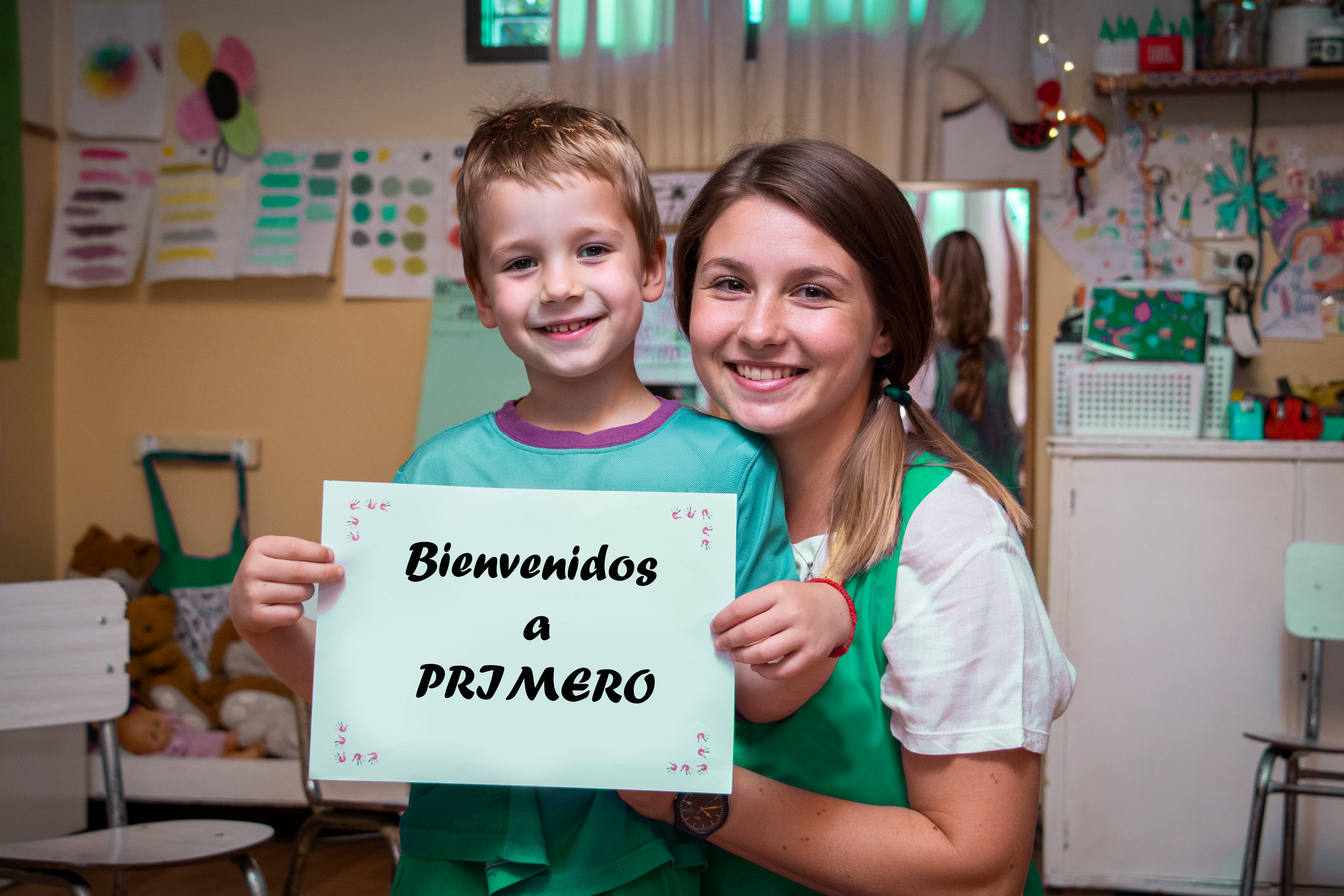 Alumno y docente con cartel de bienvenida en el aula, primer día de clases